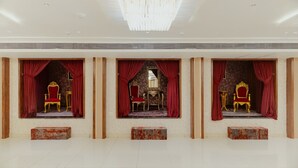 A spacious room with three ornate chairs and red curtains, a chandelier, and a tiled floor. - Hotel Ratan Mahal (Datia)