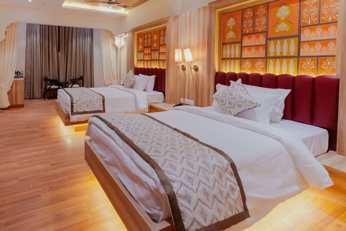 A hotel room with two beds, wooden flooring, a large window with curtains, a seating area with a table, and a decorative wall with patterned panels.