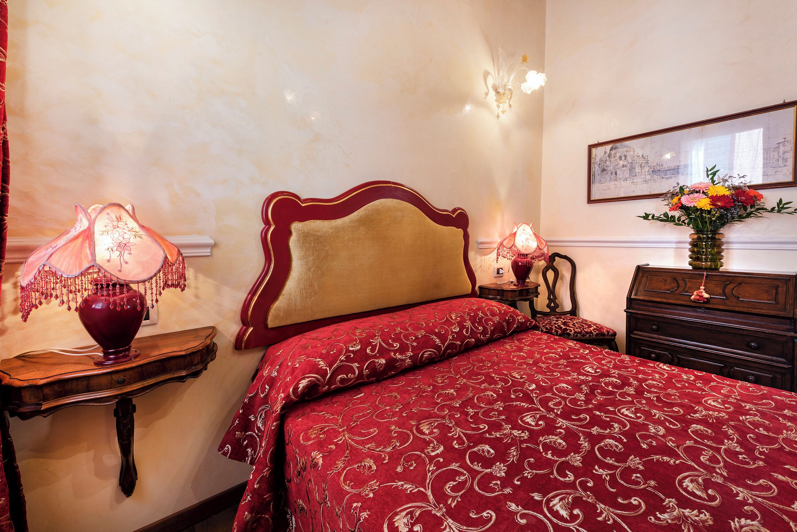 A bedroom with a large bed, a nightstand with a lamp, a dresser, and a framed picture on the wall.