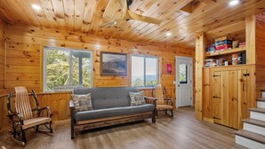A cozy cabin interior with a sofa, rocking chairs, wooden walls, and a staircase. - Fantastic 3-bedroom with lake views, fishing, hiking, skiing and snowmobiling! (Alexandria)