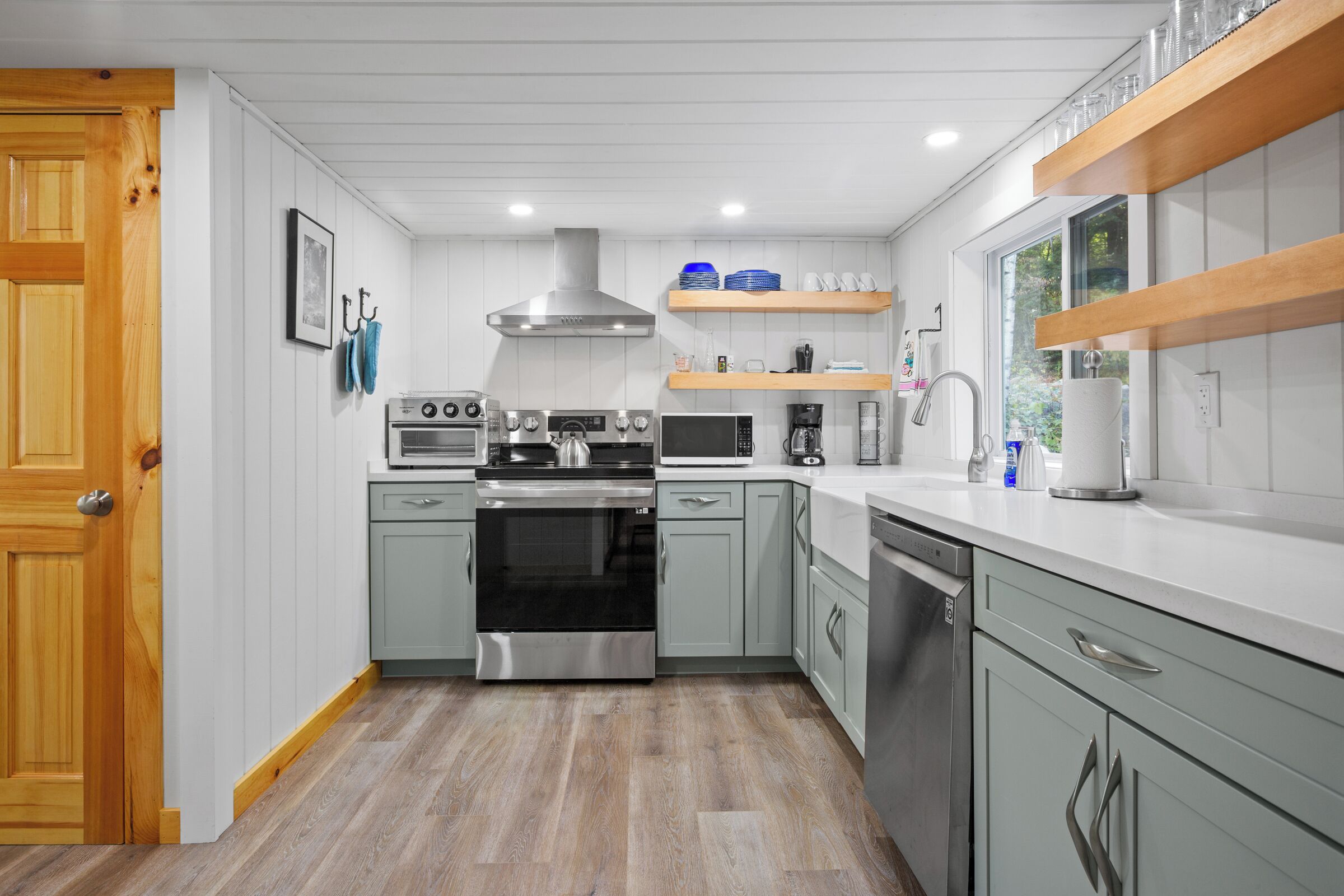 Una cocina moderna con armarios grises, electrodomésticos de acero inoxidable y repisas de madera.