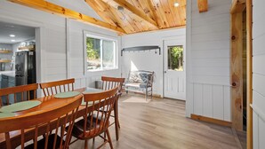 A modern kitchen with white paneling, wooden ceiling beams, and a dining area with wooden chairs and a table. - Fantastic 3-bedroom with lake views, fishing, hiking, skiing and snowmobiling! (Alexandria)