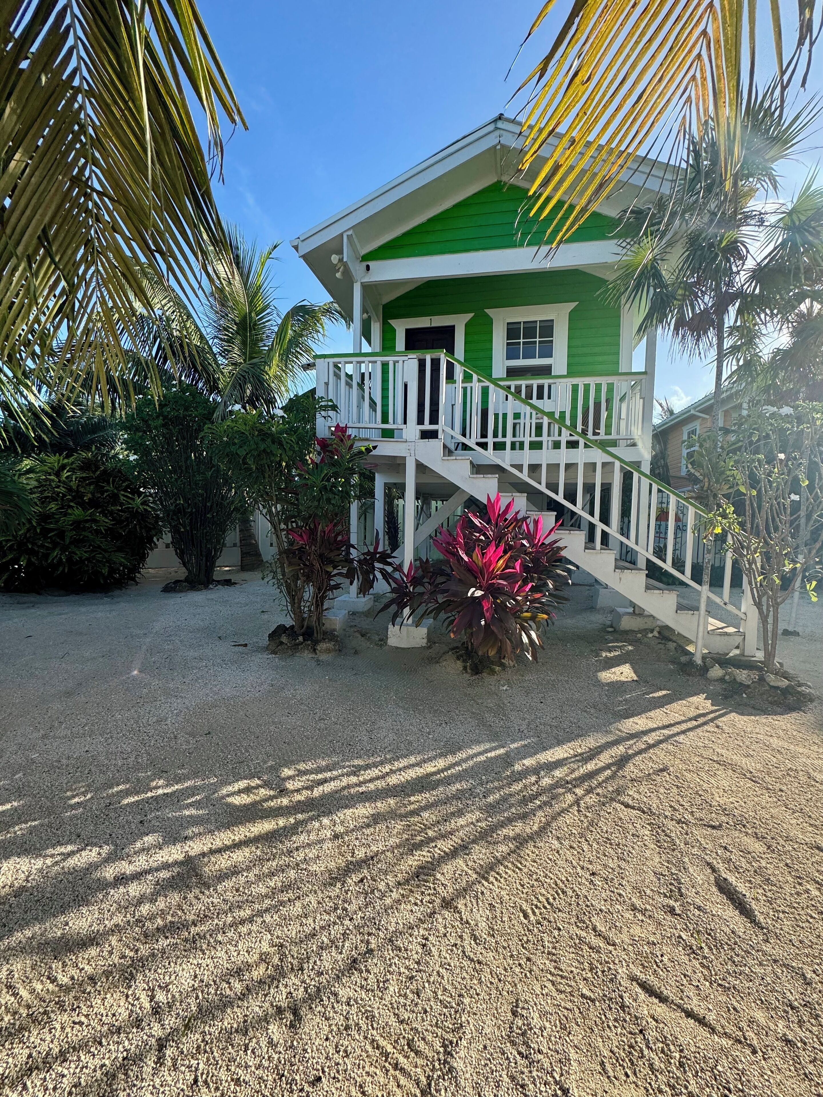 A two-story house with a green and white exterior, a white staircase, and a gravel driveway.