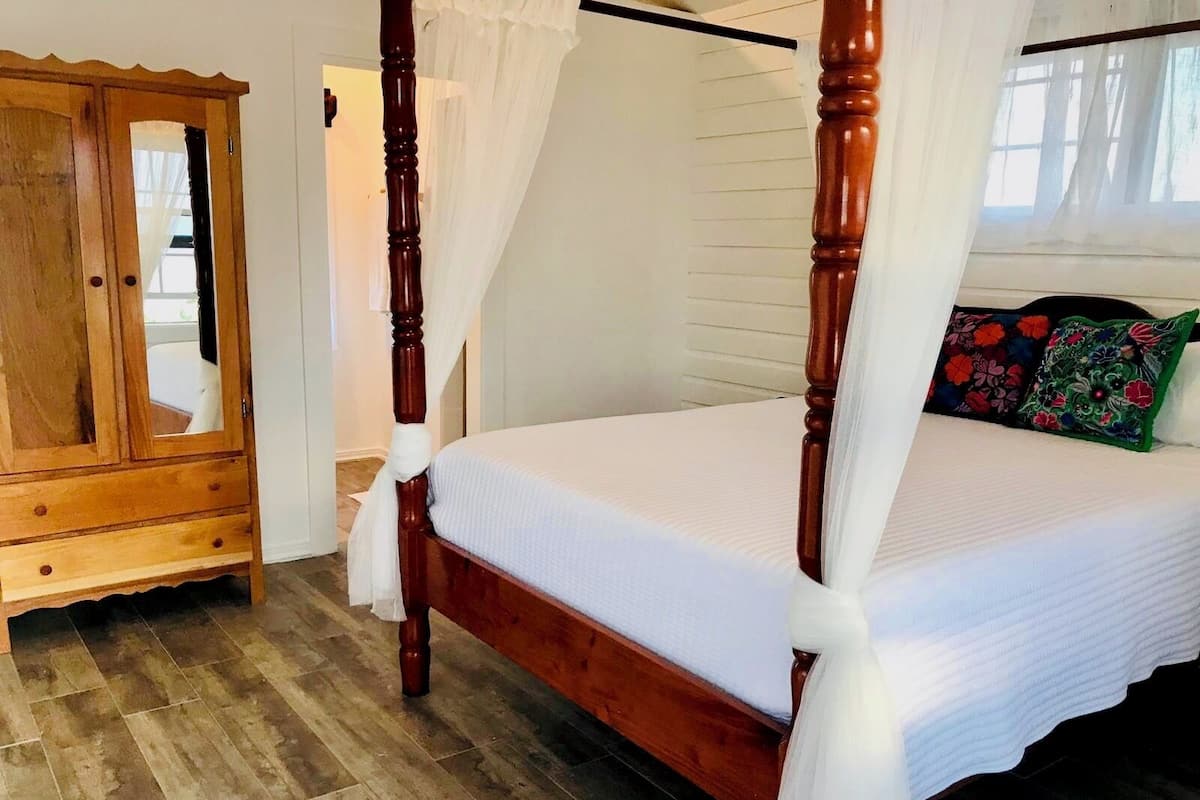 A four-poster bed with a canopy, a wooden wardrobe, and a window with curtains.