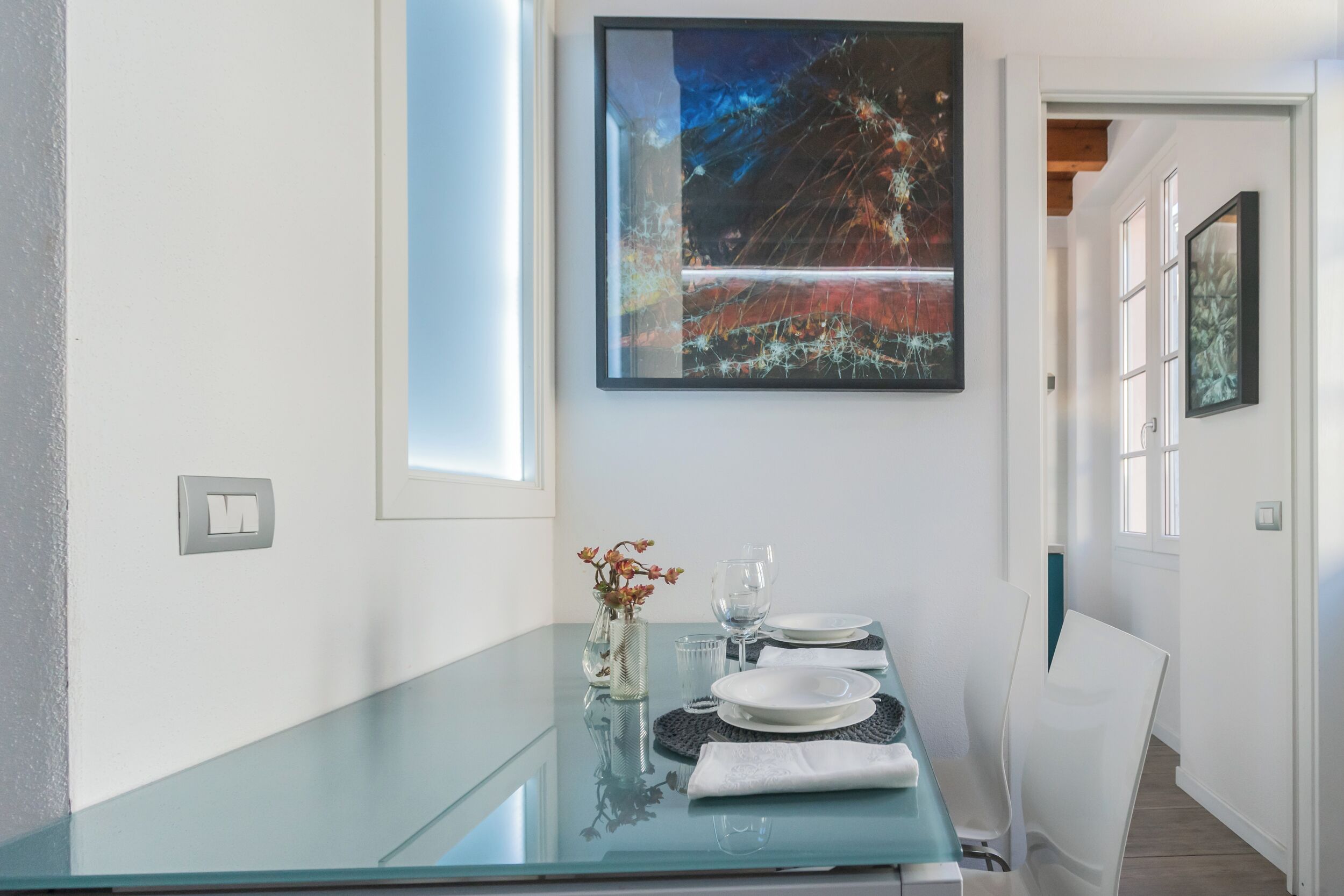 A modern dining area with a glass table, white plates, and a vase with flowers.
