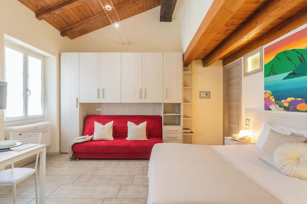 A bedroom with a red sofa, white bed, and a painting on the wall.