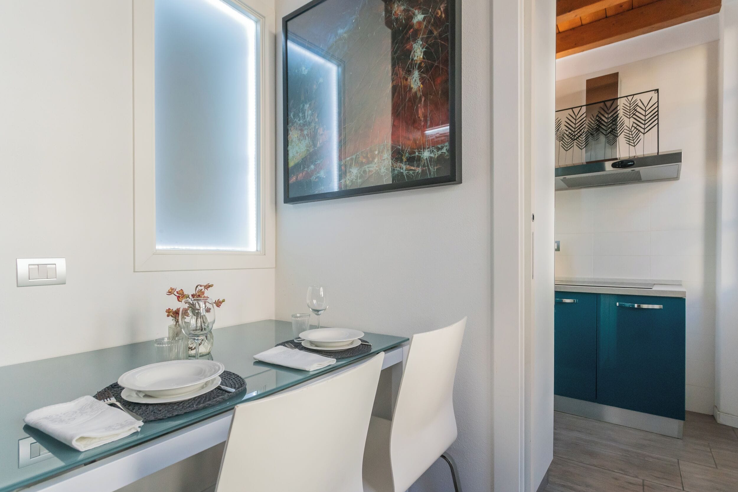 A dining area with a glass table, white chairs, and a painting on the wall.