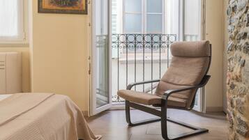 Une pièce comprenant un lit, une chaise, un balcon avec une rambarde en métal et un mur en pierre.