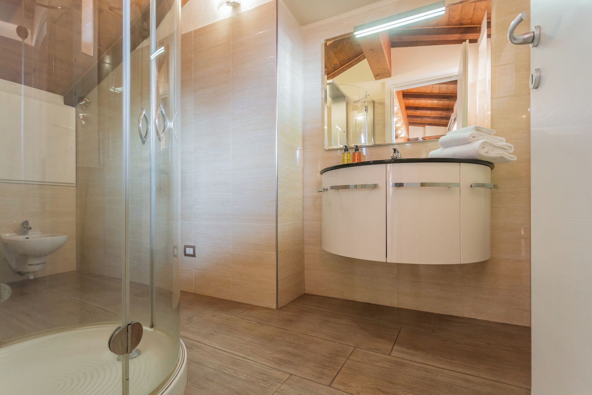A modern bathroom with a glass shower enclosure, a white sink with a mirror above, and a wooden ceiling.