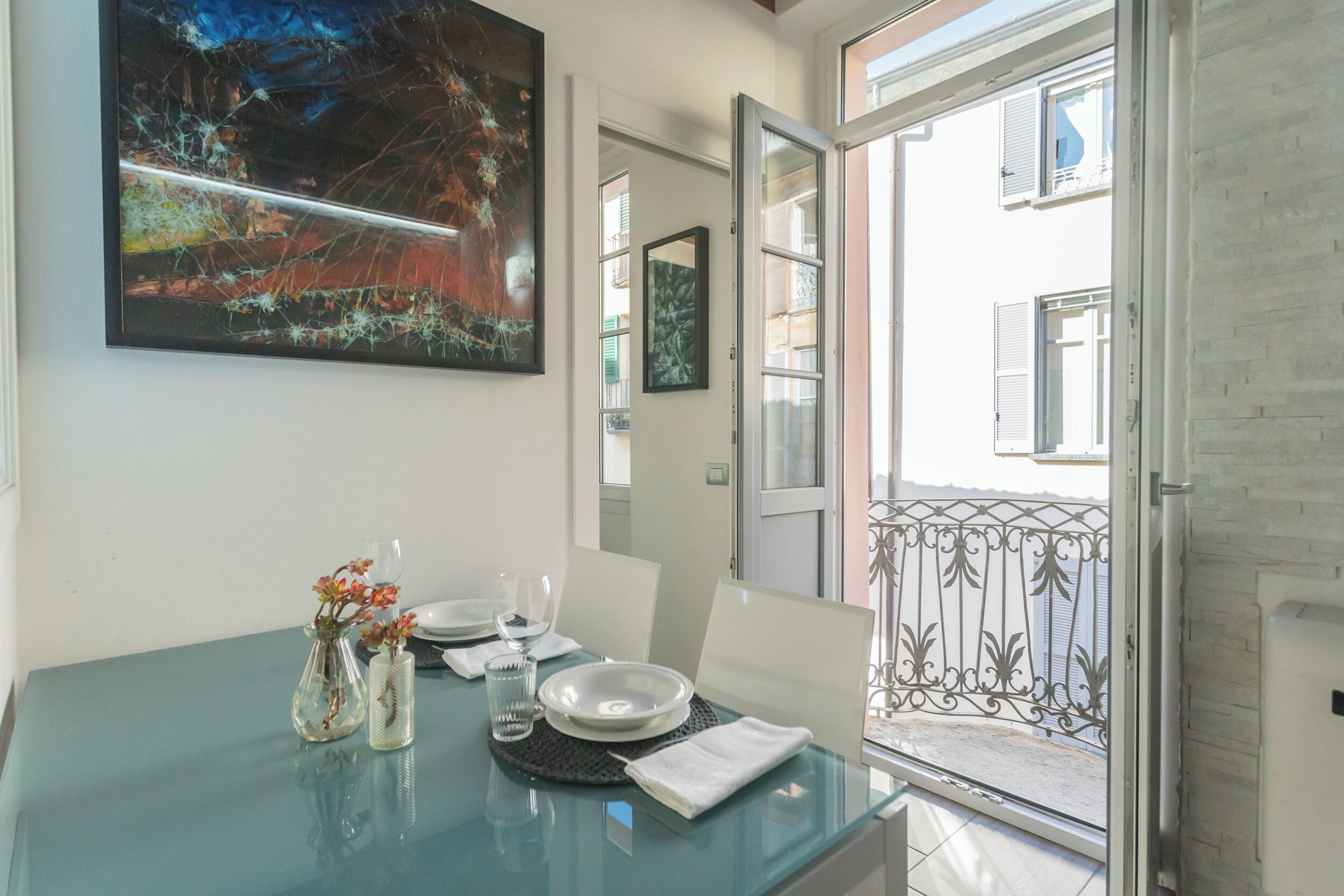A dining area with a glass table, two vases with flowers, and a painting on the wall.