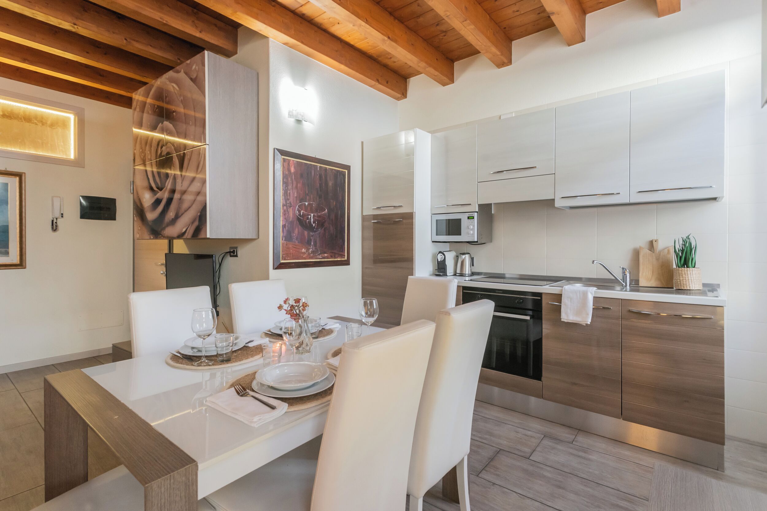 Una cucina moderna con mobili bianchi, un forno a microonde e un lavello. Un tavolo da pranzo è apparecchiato con piatti e bicchieri.