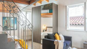 Un soggiorno moderno con una scala, un divano, un letto e una finestra vista su un tetto piastrellato.