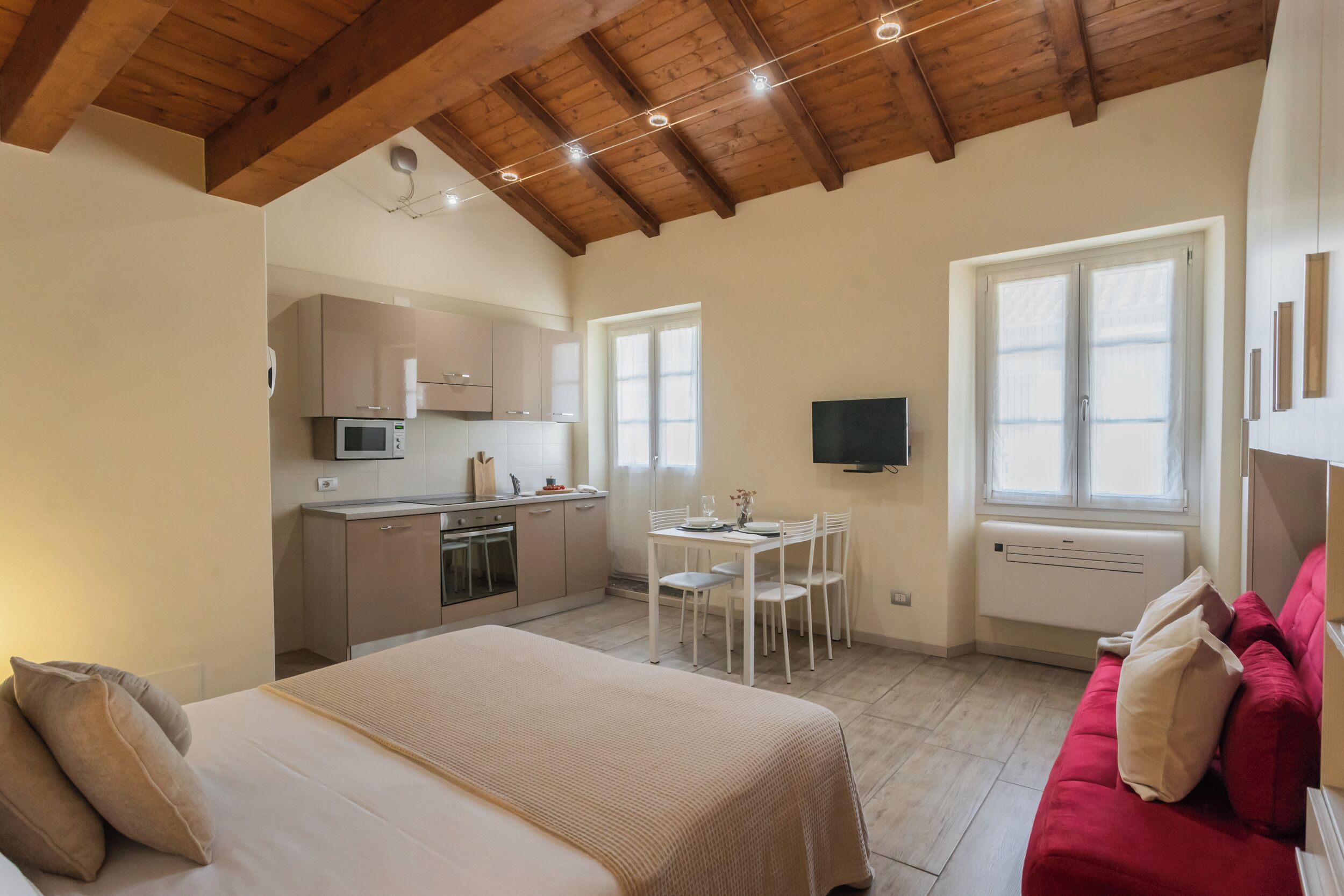 A compact room with a bed, a red couch, a dining table, and a kitchenette.