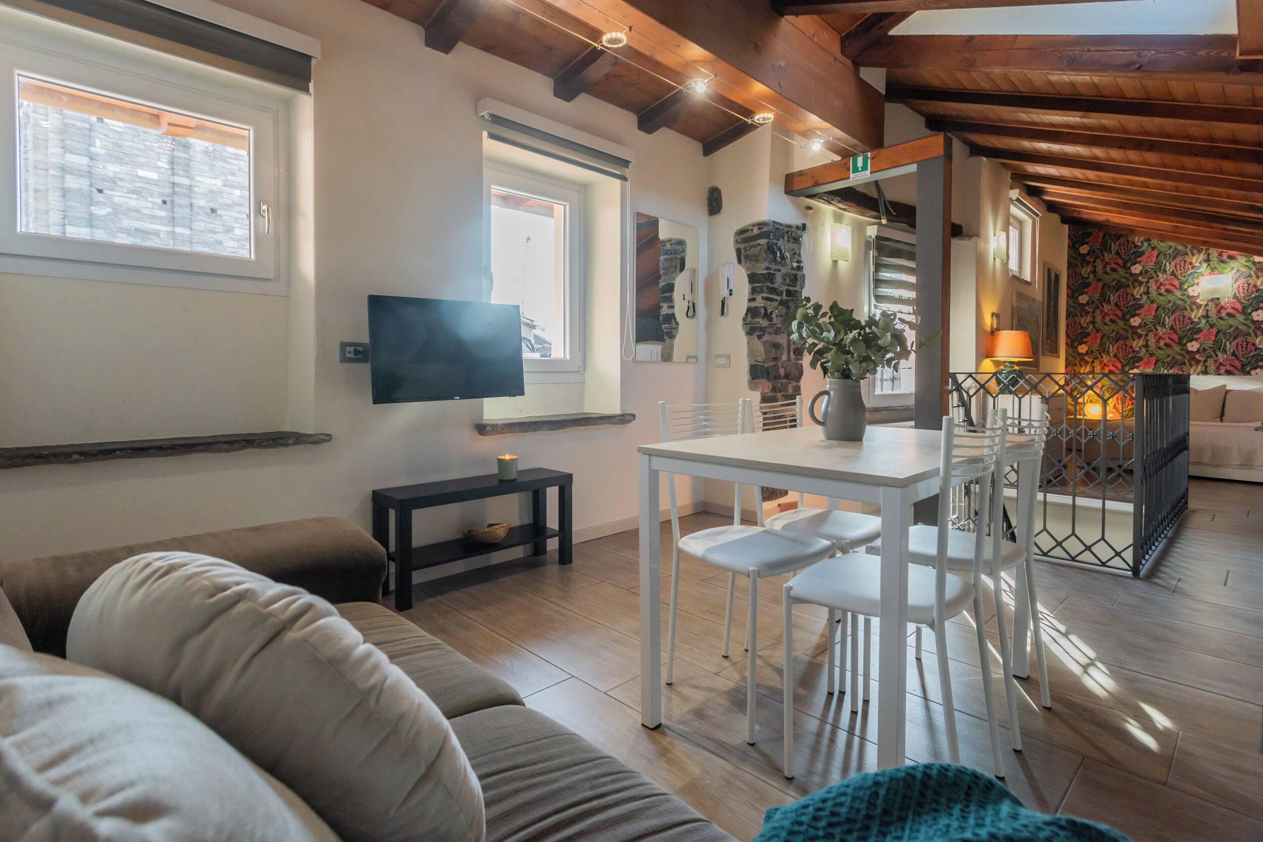 A living room with a sofa, a dining table with chairs, a TV, and a stone wall.