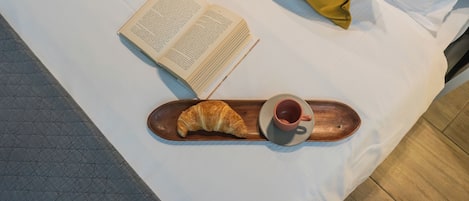 A bed with a book, a croissant, and a cup on a tray.