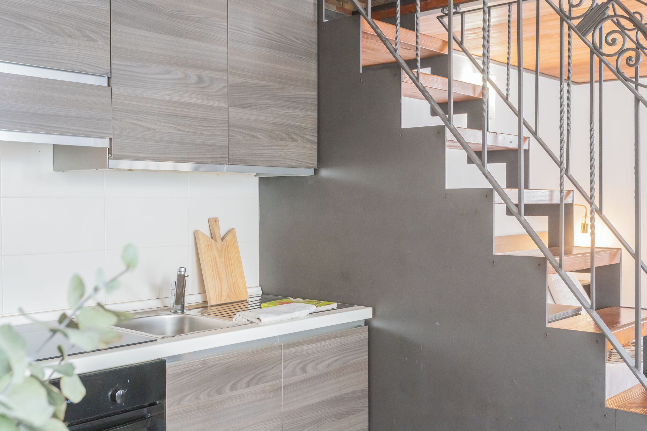 A modern kitchen with grey cabinetry, a stainless steel sink, and a wooden cutting board.