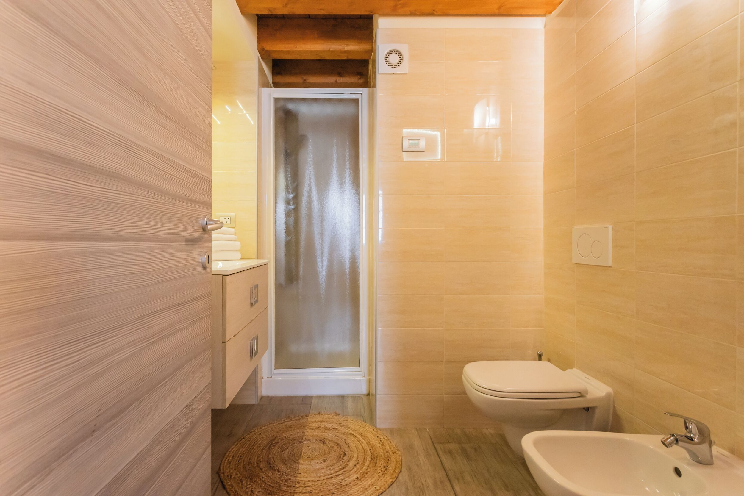 Ein kleines Badezimmer mit Holztür, Dusche, Toilette und Waschbecken.