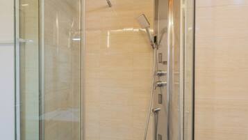 Eine begehbare Dusche mit Glaswänden, einer Handbrause und einer fest installierten Bedienfeld.