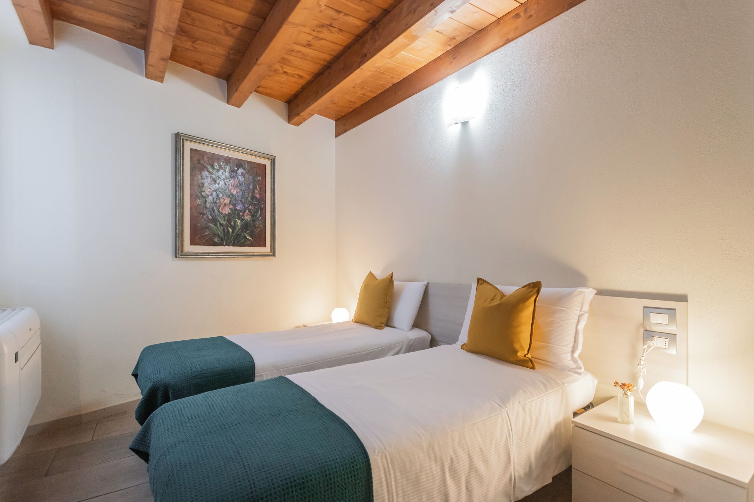 A bedroom with two beds, a nightstand, a bedside table with a lamp, and a painting on the wall.