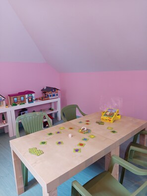Ett rum med ett träbord, gröna stolar och en rosa vägg. På bordet står det leksaker och en leksakslåda.