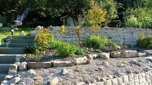 A stone retaining wall with a garden area, steps leading up to a building, and a tree in the background. - 3-star rated house (sleeps 4) with private spa and garden (Bouvigny-Boyeffles)