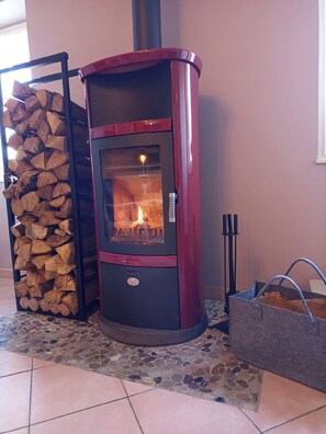 Ein Kaminofen mit Glasfront, ein Holzstapel und ein Boden mit Steinfliesen.