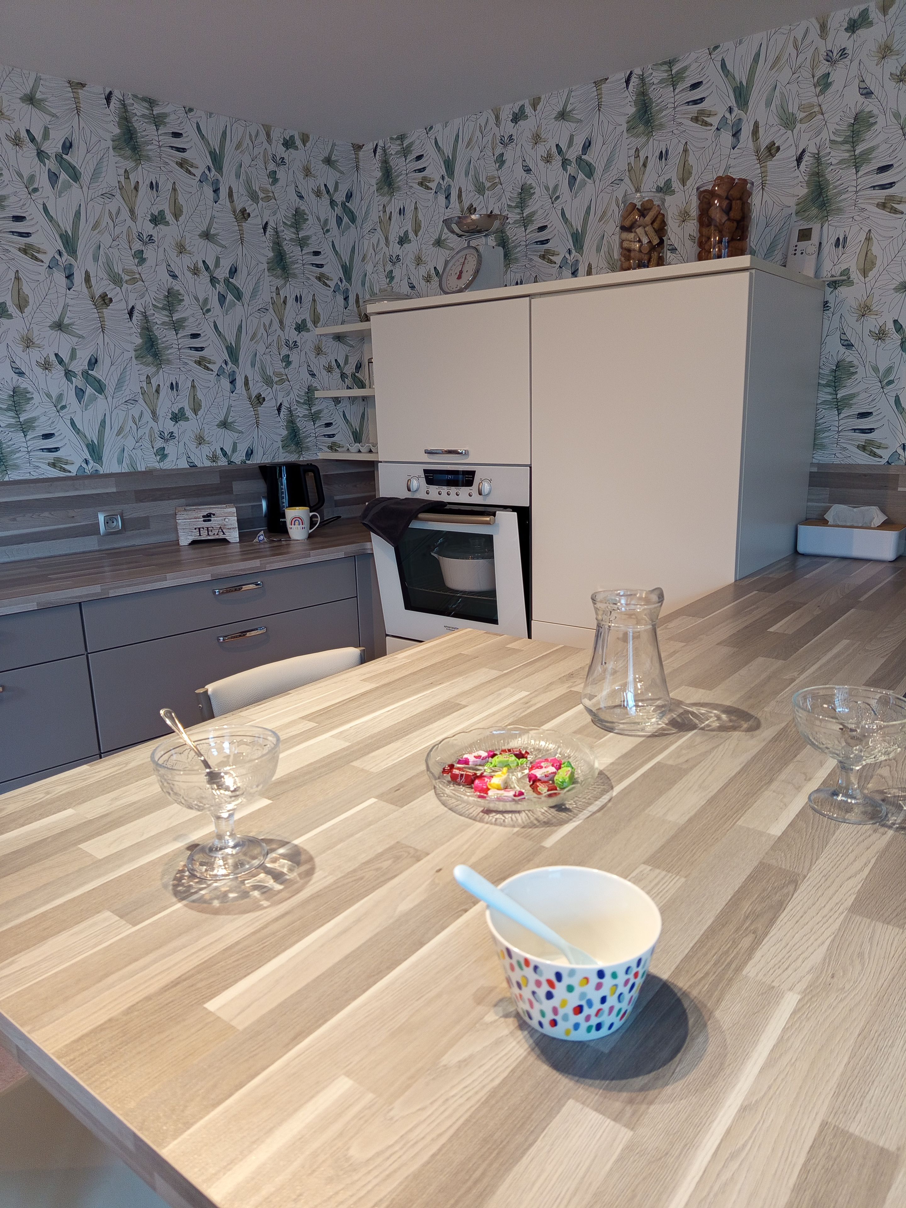 A modern kitchen with a wooden countertop, a kettle, a coffee maker, and a tea box.