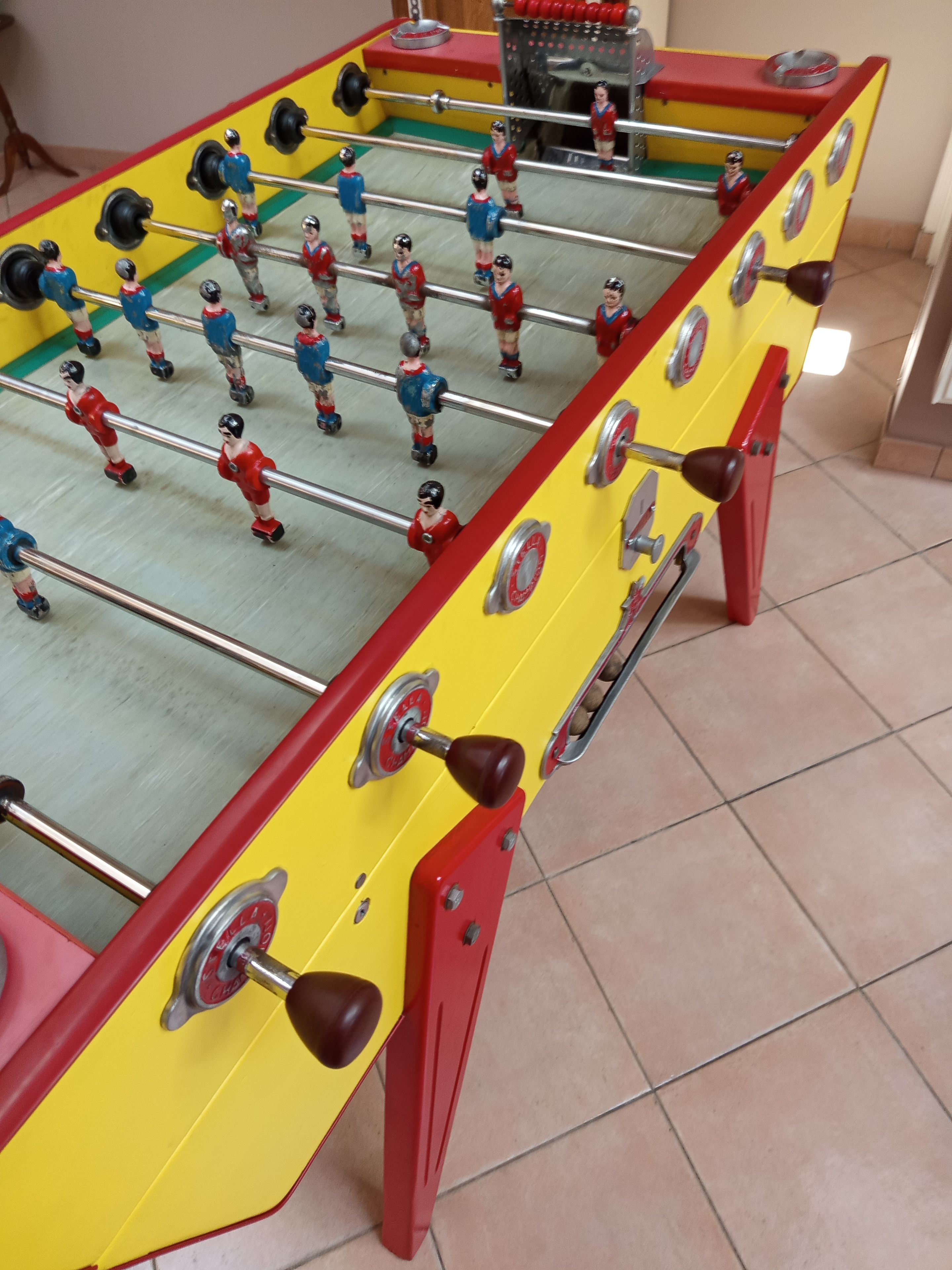 Ein Kicker mit roten und gelben Akzenten, ausgestattet mit Metallstangen und Spielfiguren.