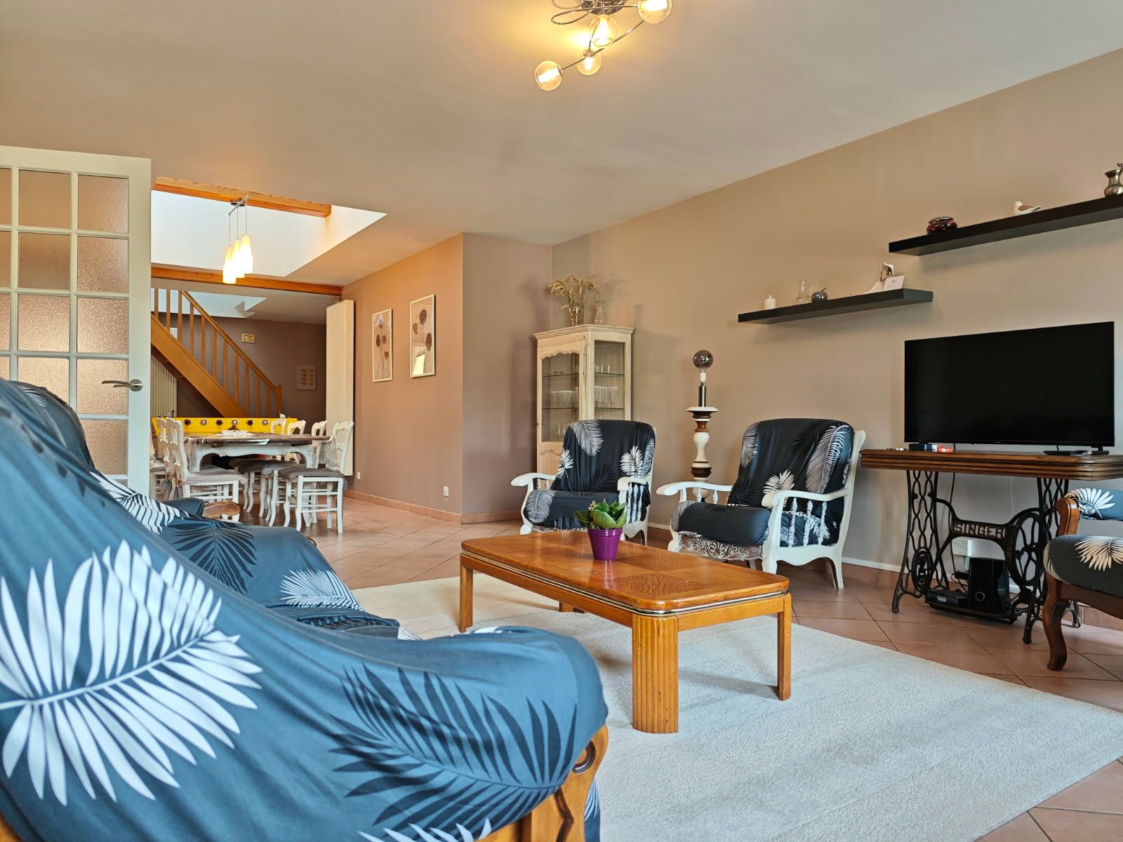 Een woonkamer met een bank, fauteuils, een salontafel, een televisie en een eethoek met stoelen en een tafel.