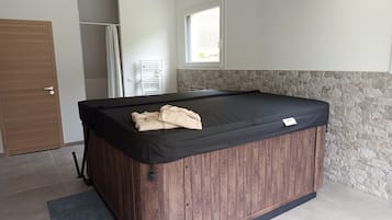 A room with a wooden spa tub, a stone wall, and a window.