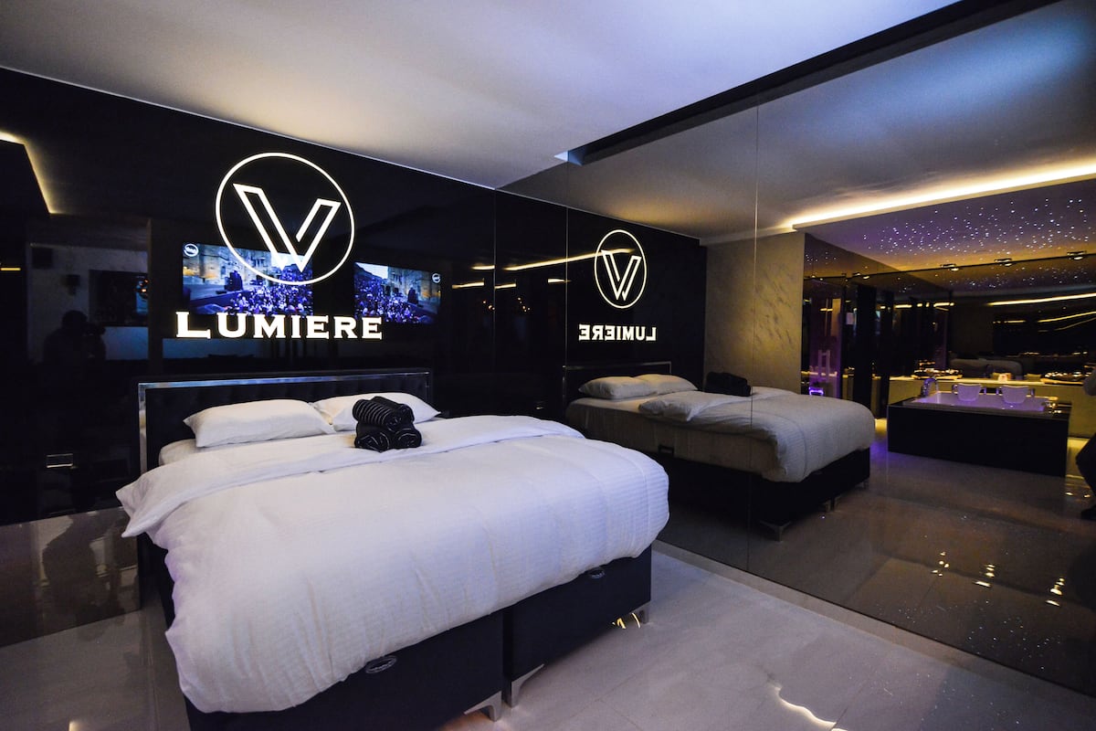 A modern hotel room with a large bed, a smaller bed, and a TV. The room has a starry ceiling and a logo on the wall.