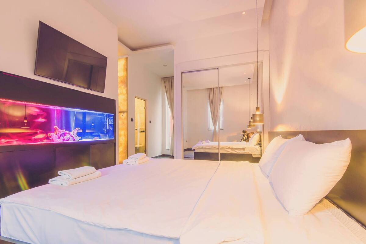 A hotel room with a large bed, a flat-screen TV mounted on the wall, and a wall-mounted aquarium.