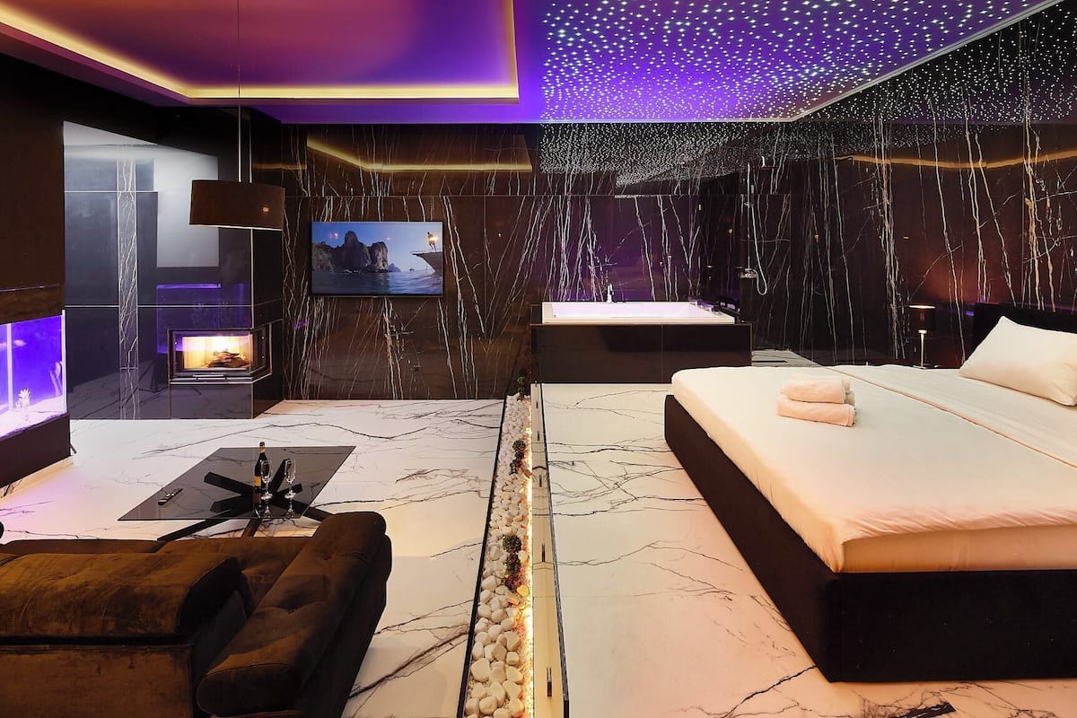 A modern bedroom with a large bed, a TV, a fireplace, and a marble floor.