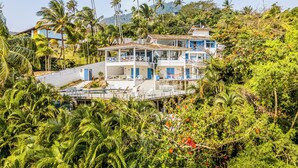 A multi-story building with balconies, surrounded by dense tropical vegetation and palm trees. - Casa da Imperatriz (Ilhabela)