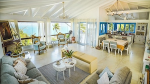 A spacious living area with a sofa, dining table, and chairs, a kitchen with white cabinets, and a view of the ocean. - Casa da Imperatriz (Ilhabela)