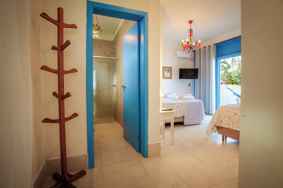 Une chambre d’hôtel avec une porte bleue, un porte-manteau en bois, un lit recouvert d’une courtepointe à motifs floraux, une télévision et une fenêtre avec des rideaux.
