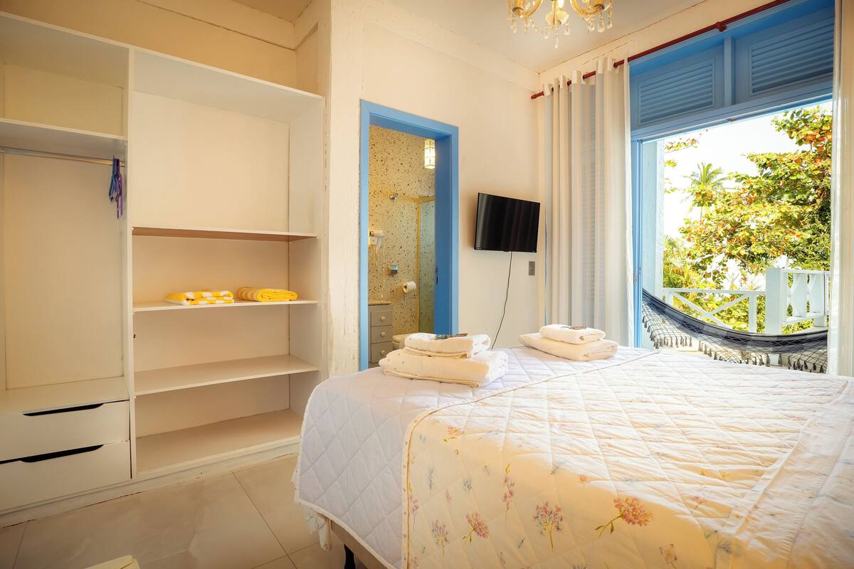 Une chambre à coucher comprenant un lit, une armoire, un téléviseur et une fenêtre donnant sur un paysage verdoyant.