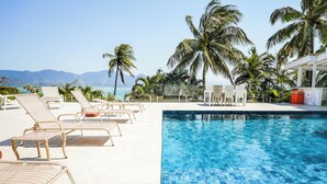 A poolside area with lounge chairs and palm trees, overlooking a body of water and mountains. - Casa da Imperatriz (Ilhabela)