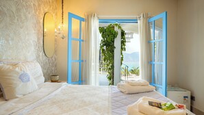 A hotel room with a large bed, a bedside table, a mirror, and a view of the sea through open blue doors. - Casa da Imperatriz (Ilhabela)