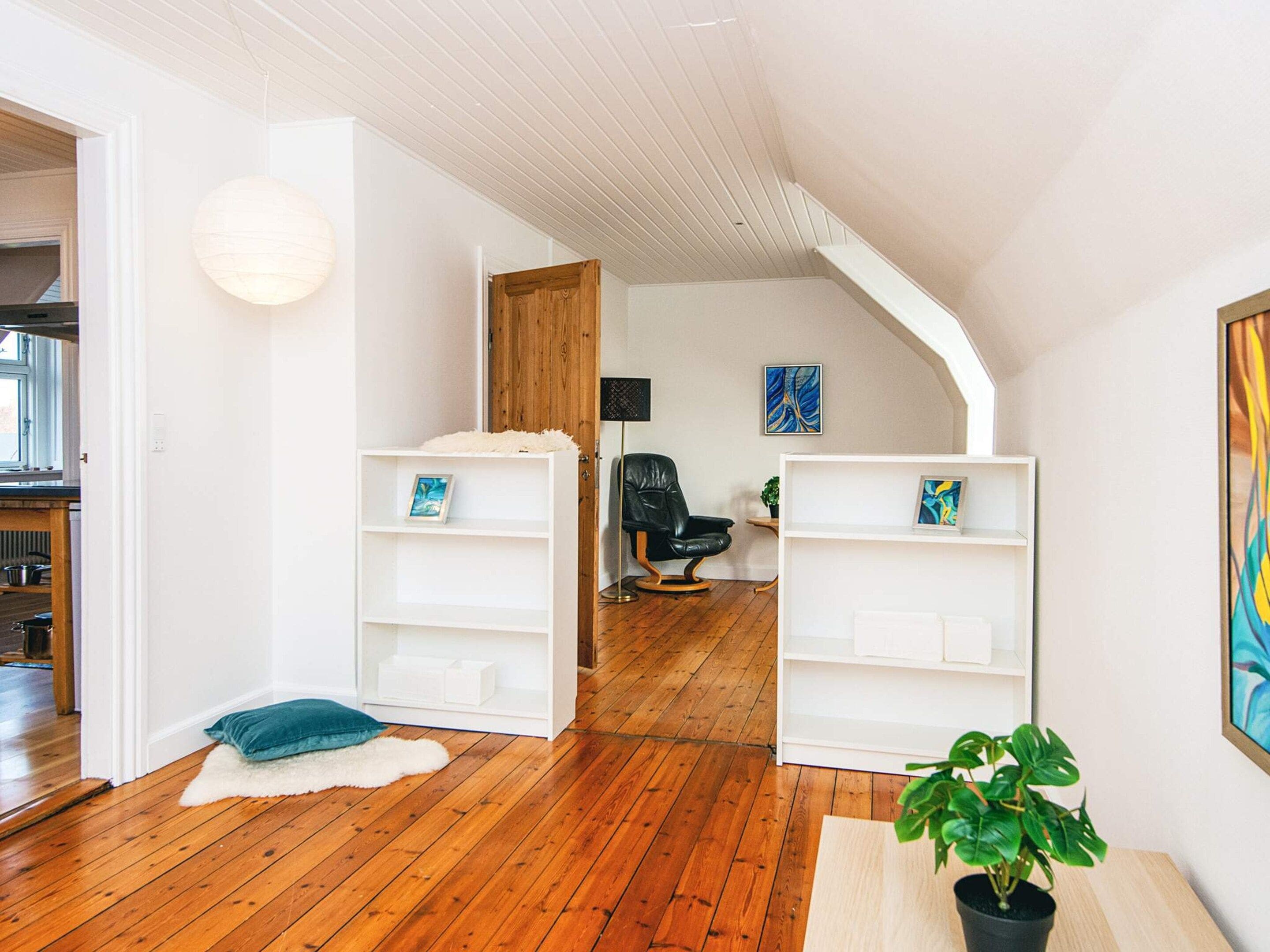 A spacious room with wooden flooring, white shelving units, a black leather chair, and a potted plant.