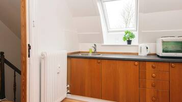 A kitchen with a window, a radiator, wooden cabinets, a microwave, and a potted plant.