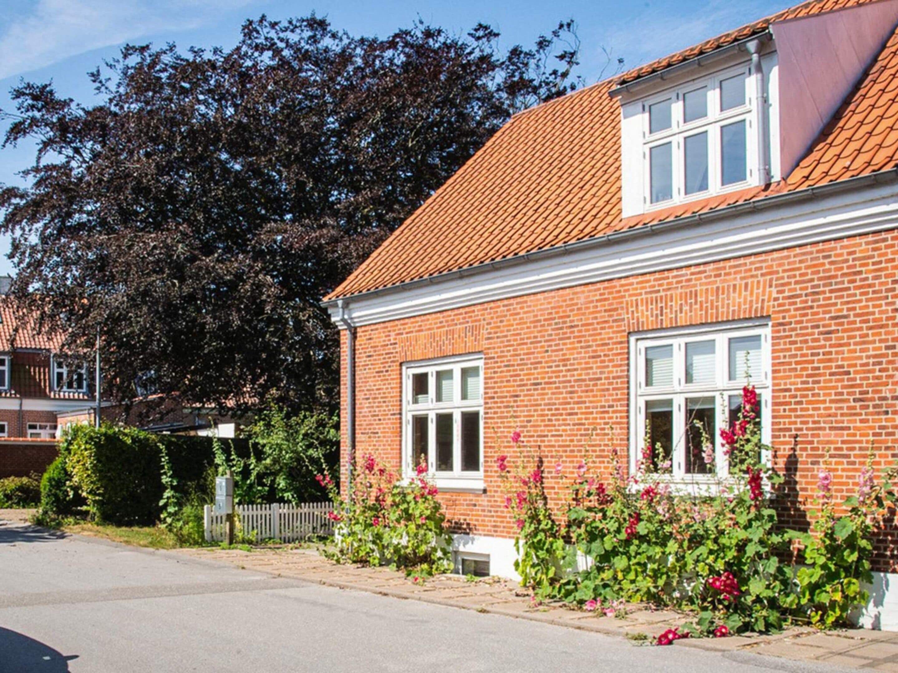 A two-story brick house with a red-tiled roof, white-framed windows, and a white picket fence.
