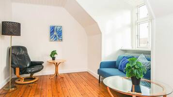 Uma sala de estar moderna com uma poltrona de couro preta, um sofá azul, uma mesa de centro de vidro e uma mesa redonda pequena com uma planta.