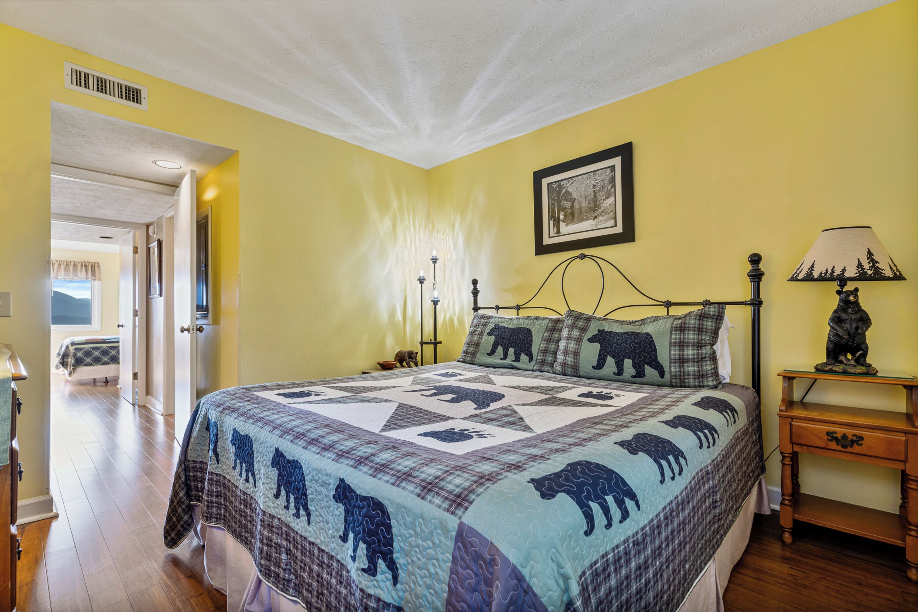 Un dormitorio con cama, mesita de noche, lámpara y un cuadro en la pared.