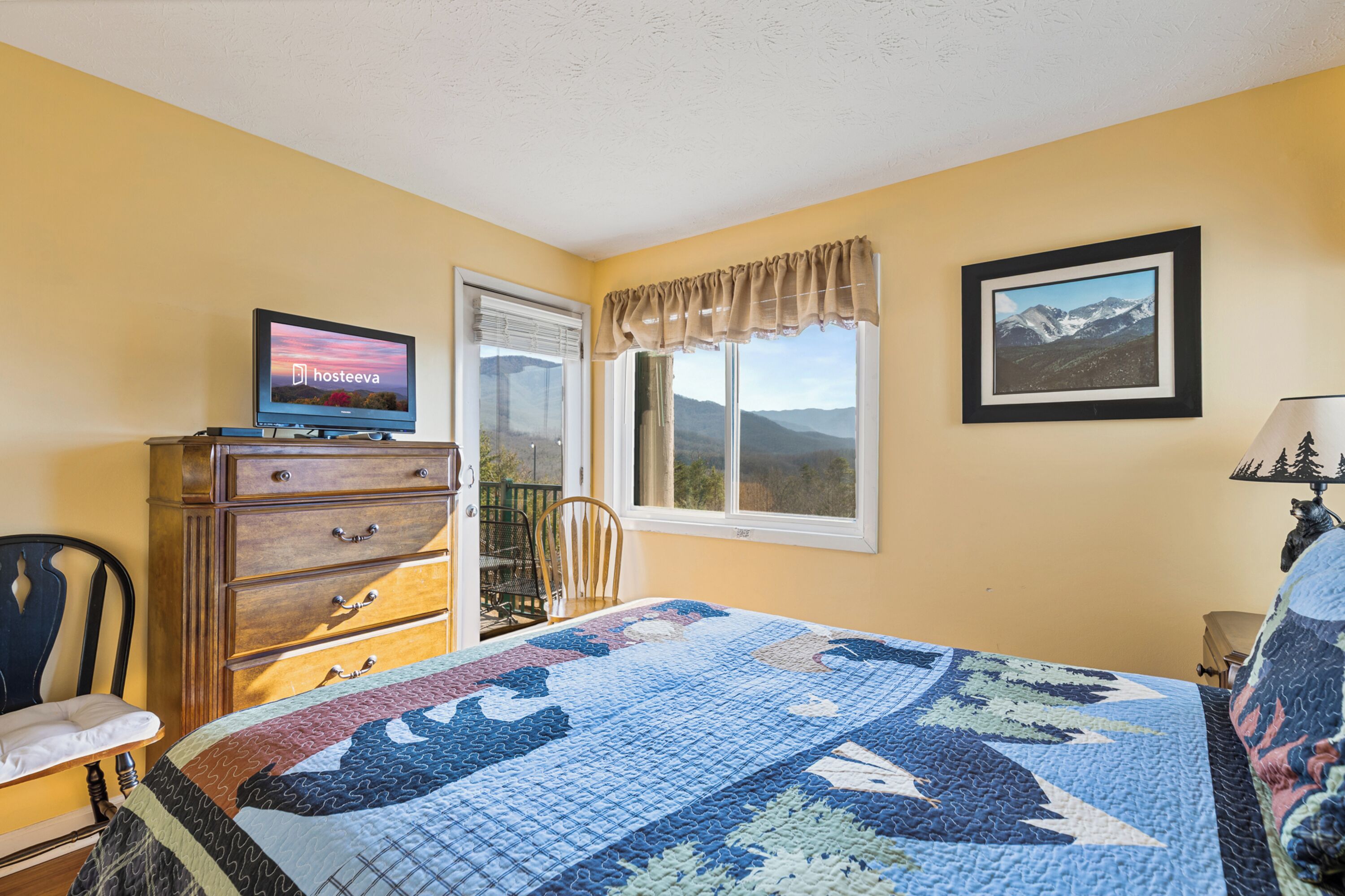 A bedroom with a bed, dresser, TV, window, and framed picture.