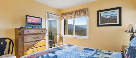 A bedroom with a bed, dresser, TV, window, and framed picture.