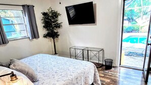 A bedroom with a bed, a desk, a ceiling fan, a TV, and a sliding glass door leading to an outdoor area.