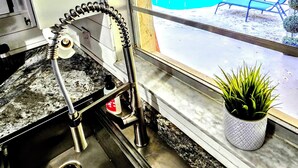 A kitchen with a sink, a window with a view of a swimming pool, and a potted plant on the windowsill.