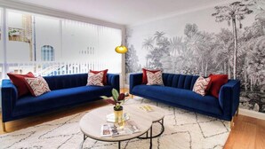 Una sala de estar con dos sofás azules, una mesa de centro redonda y un mural tropical en la pared.