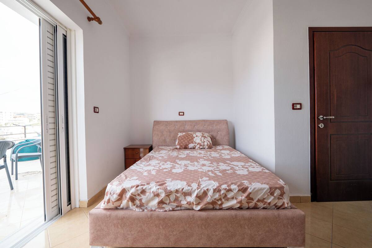 A bedroom with a bed, a wooden door, and a sliding glass door leading to an outdoor area.
